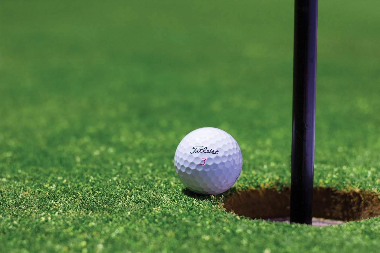 A Titleist golf ball on a golf course near a golf hole and flag