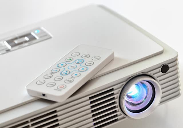 A white projector with its remote control on a white surface