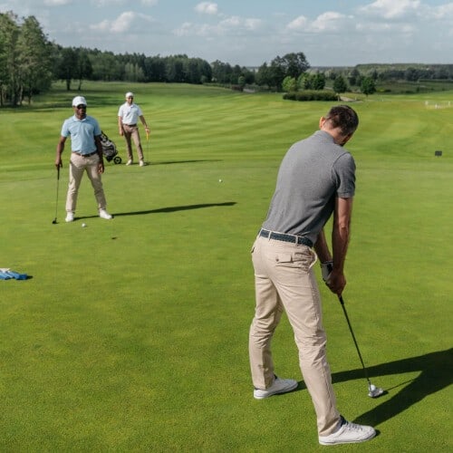 A golfer getting ready for a putting shot on a golf course with two other golfers in the background 