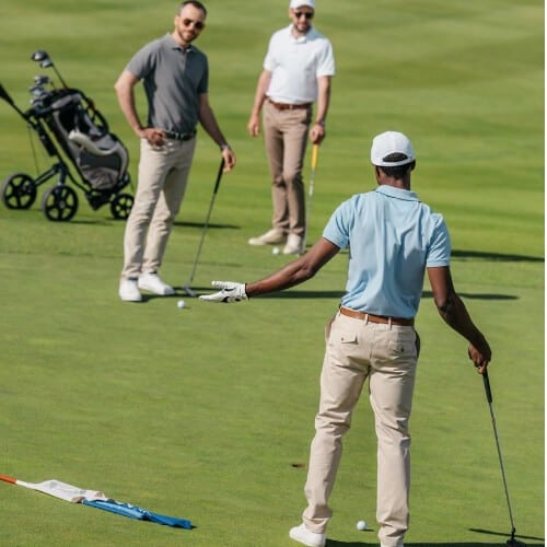 A golfer playing with friends in golf course with a golf bag and cart in the background