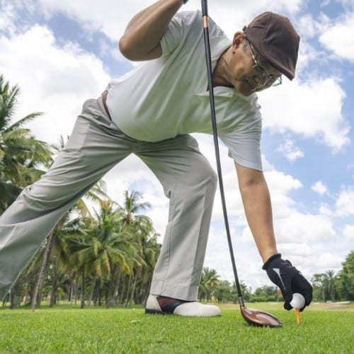 A senior golfer holding a golf club while placing golf ball and tee on the golf course