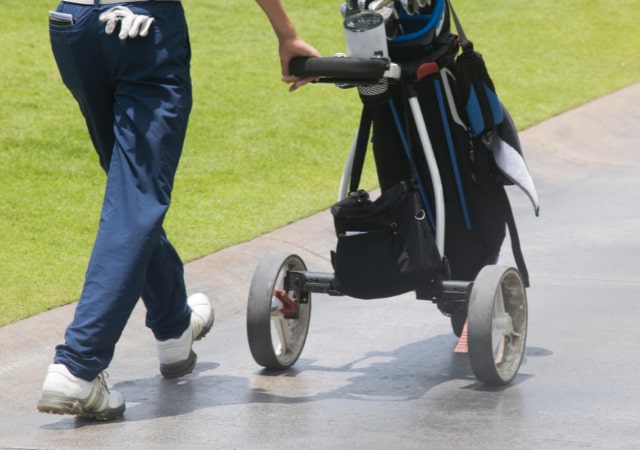 A golfer pushing the golf push cart on the pavement of a golf course