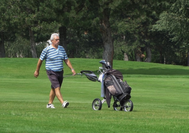 A golfer walking towards his golf push cart on the golf course while holding a golf club