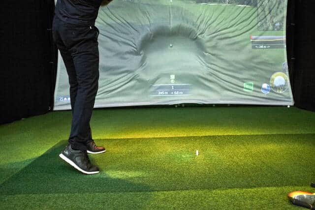 golfer practicing on an indoor golf simulator setup with projection screen and and hitting mat
