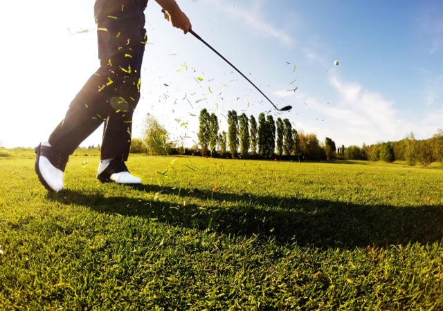 A golfer performing a chip shot on a golf course with a bunch of grass leaves in the air