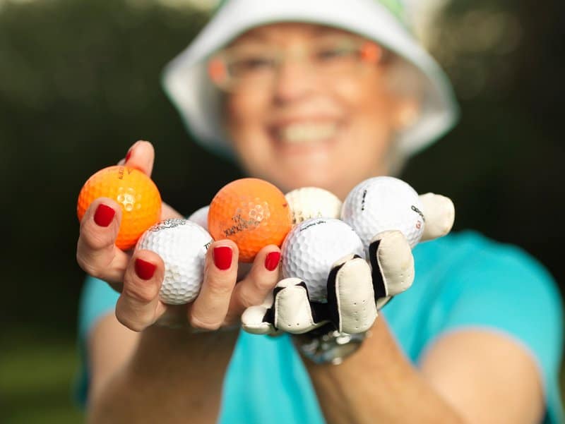 A female golfer holding a bunch of orange and white golf balls