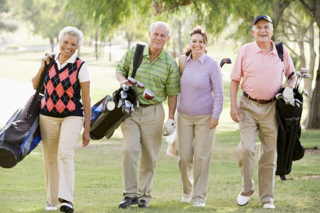 Portrait Of Four Friends Enjoying A Game Golf while carrying their golf bags