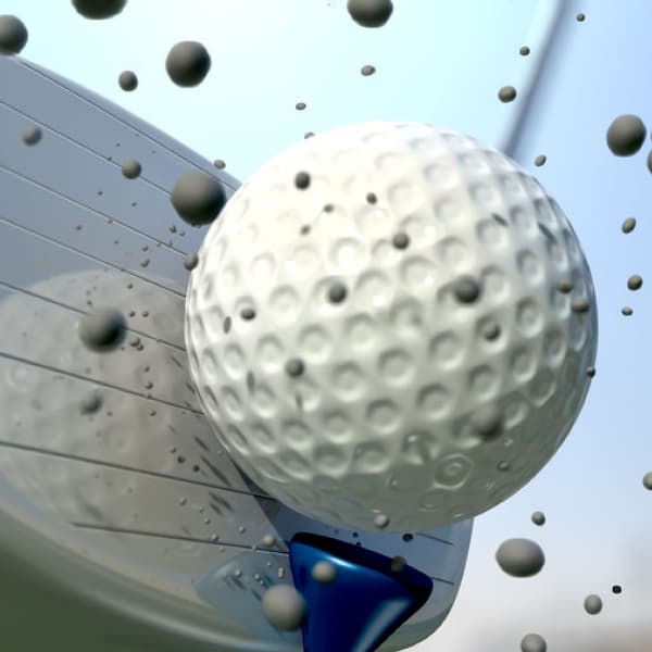 A golf ball on a golf tee being hit with a golf club with dirt in the air