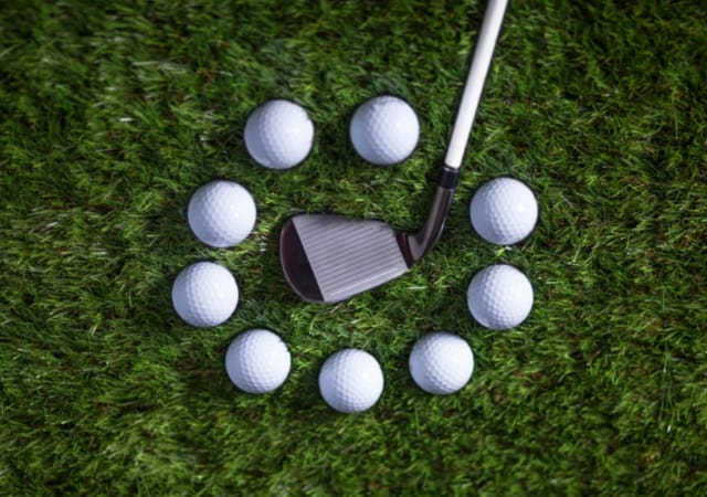 A golf club placed on the grass with nine golf balls arranged in a circle around the golf clubhead