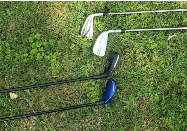 Two regular golf clubs and two hybrid golf clubs laid down on grass of a golf course