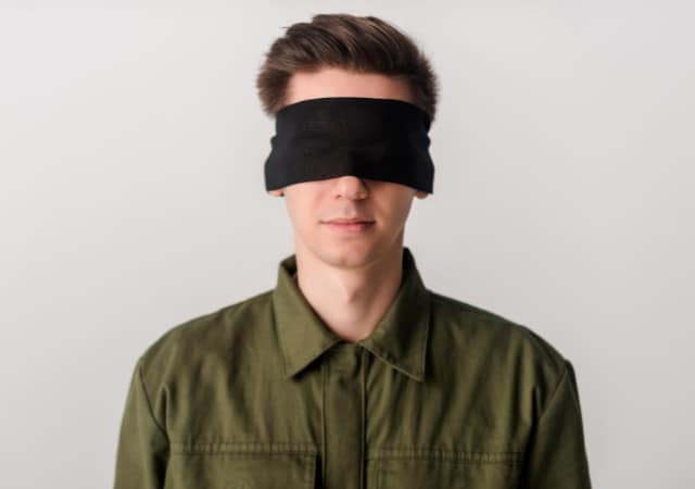 A blindfolded man on a plain white wall