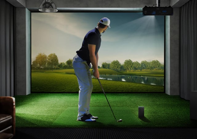 golfer practicing his golf swing using a golf simulator while holding a golf club preparing to put the golf ball