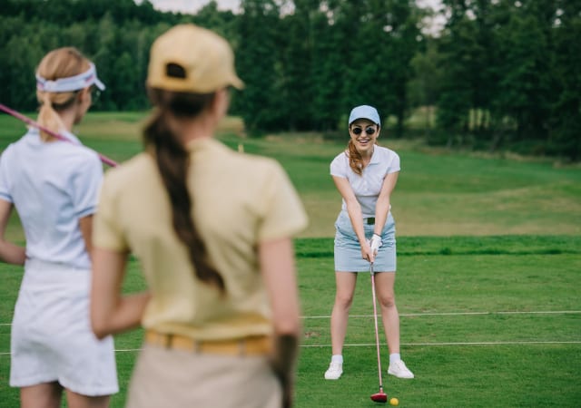 A female golfer preparing for a swing on a golf course with two of her friends watching her