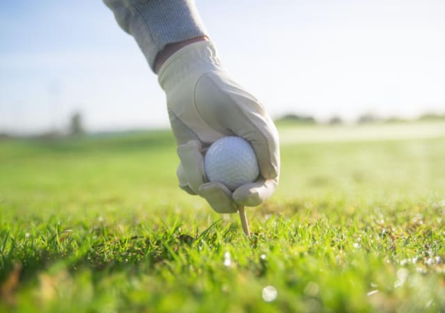 A man with a white golf club setting down a golf ball and golf tee on a golf course