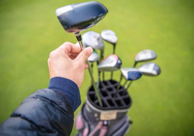 A hand holding one of the golf clubs in the golf bag on the golf course
