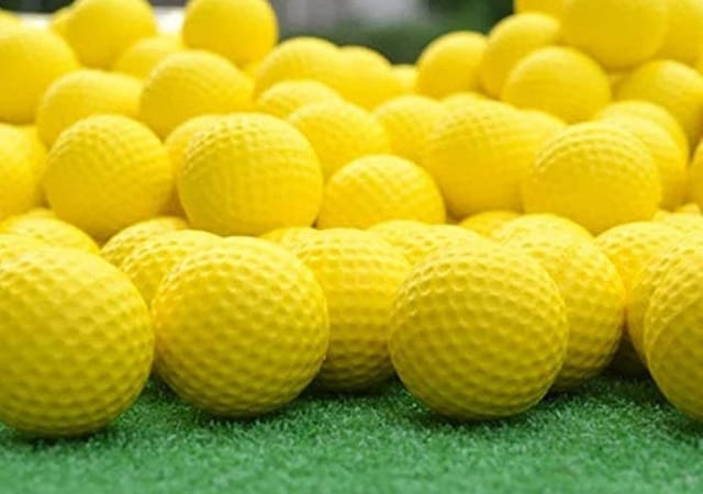A bunch of yellow foam practice golf balls on green faux grass