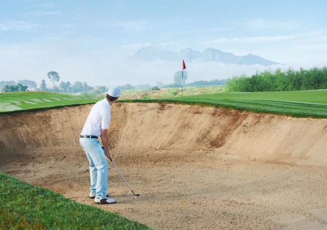 A golfer preparing for a shot inside the sand pit on a golf course