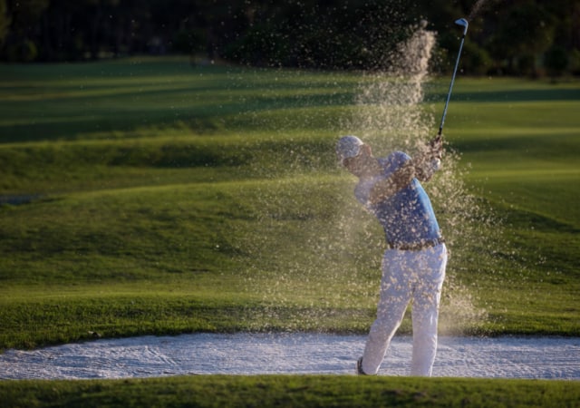 A golfer after making a bunker shot in the sand pit with sand flying in the air after the shot