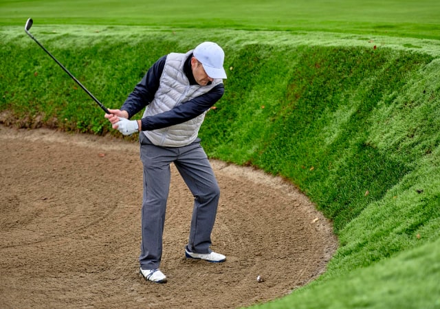 A golfer swinging his golf club to make a bunker shot in the sand pit on a golf course