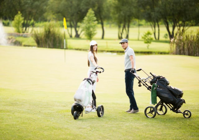 Male and female golfer holding their golf caddies on the golf course