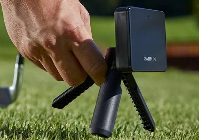 A golfer placing the Garmin Approach R10 on the ground of a golf course