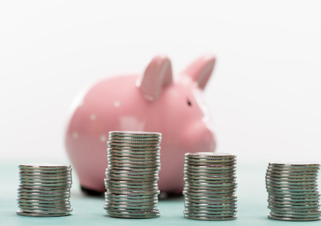 Four stacks of coins with varying height placed in front of  piggy bank on white background