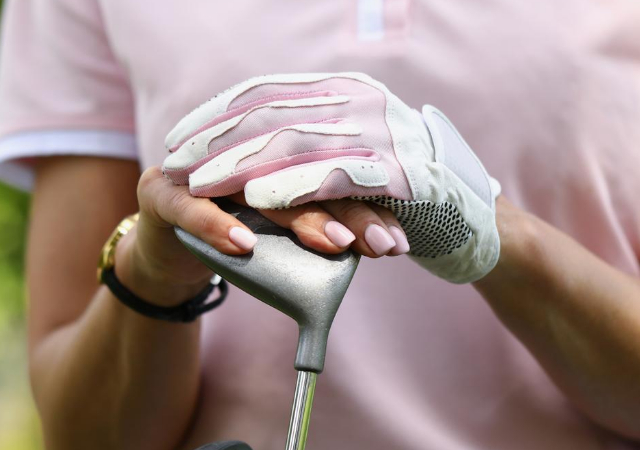 A female golfer wearing a golf glove while holding a golf club's head with two hands