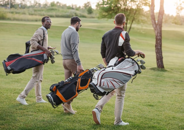 Three male golfers carrying their golf bags on the golf course