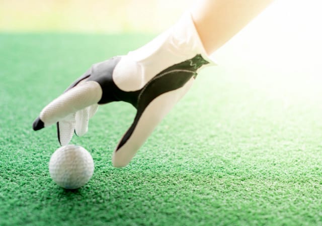A golfer wearing a golf glove reaching for a golf ball on turf