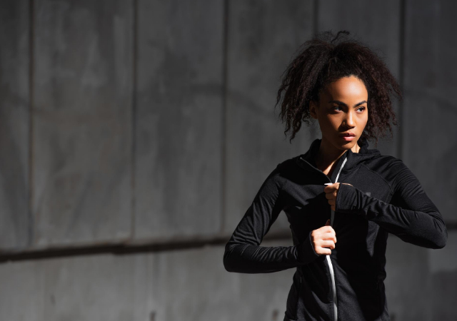 Woman zipping up her sports jacket with concrete background