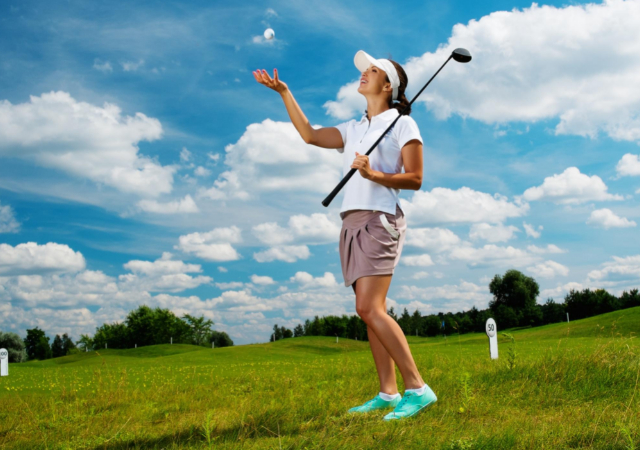 Female golfer throwing a golf ball up in the air while holding a golf club in the other hand on the golf course