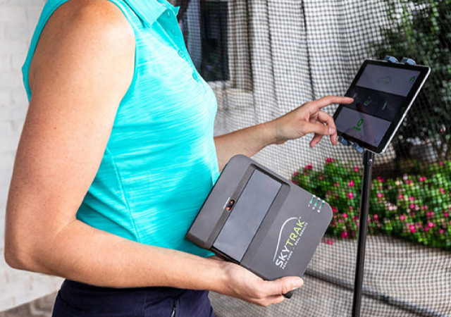 Woman holding the skytrak launch monitor while using the ipad to enter data and navigate through the skytrak simulator software